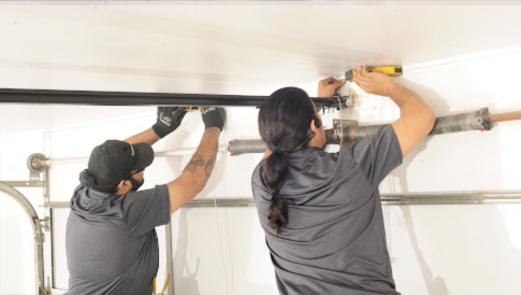 Two garage door technicians replacing a torsion spring on an overhead door